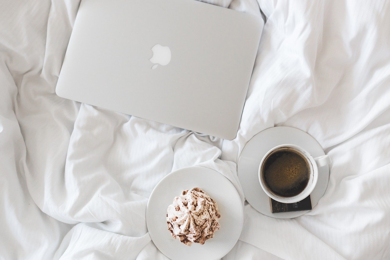 Laptop on bed with coffee and a cake