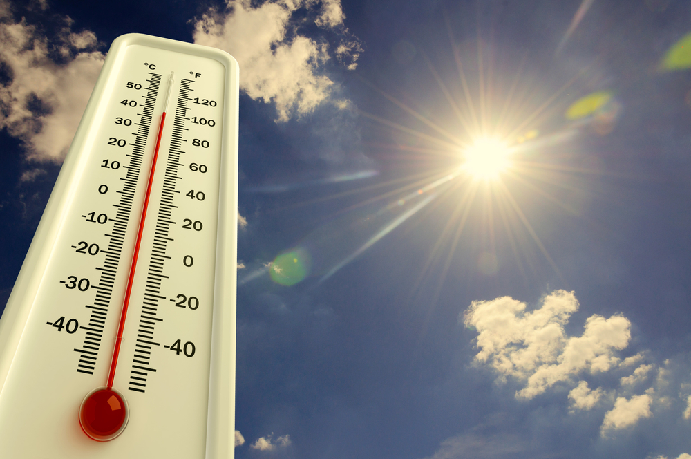 A view of a thermometer and the sun in a cloudy summer sky