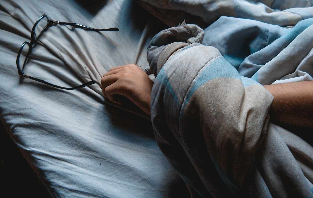 Someone sleeping in a messy mattress holding their glasses