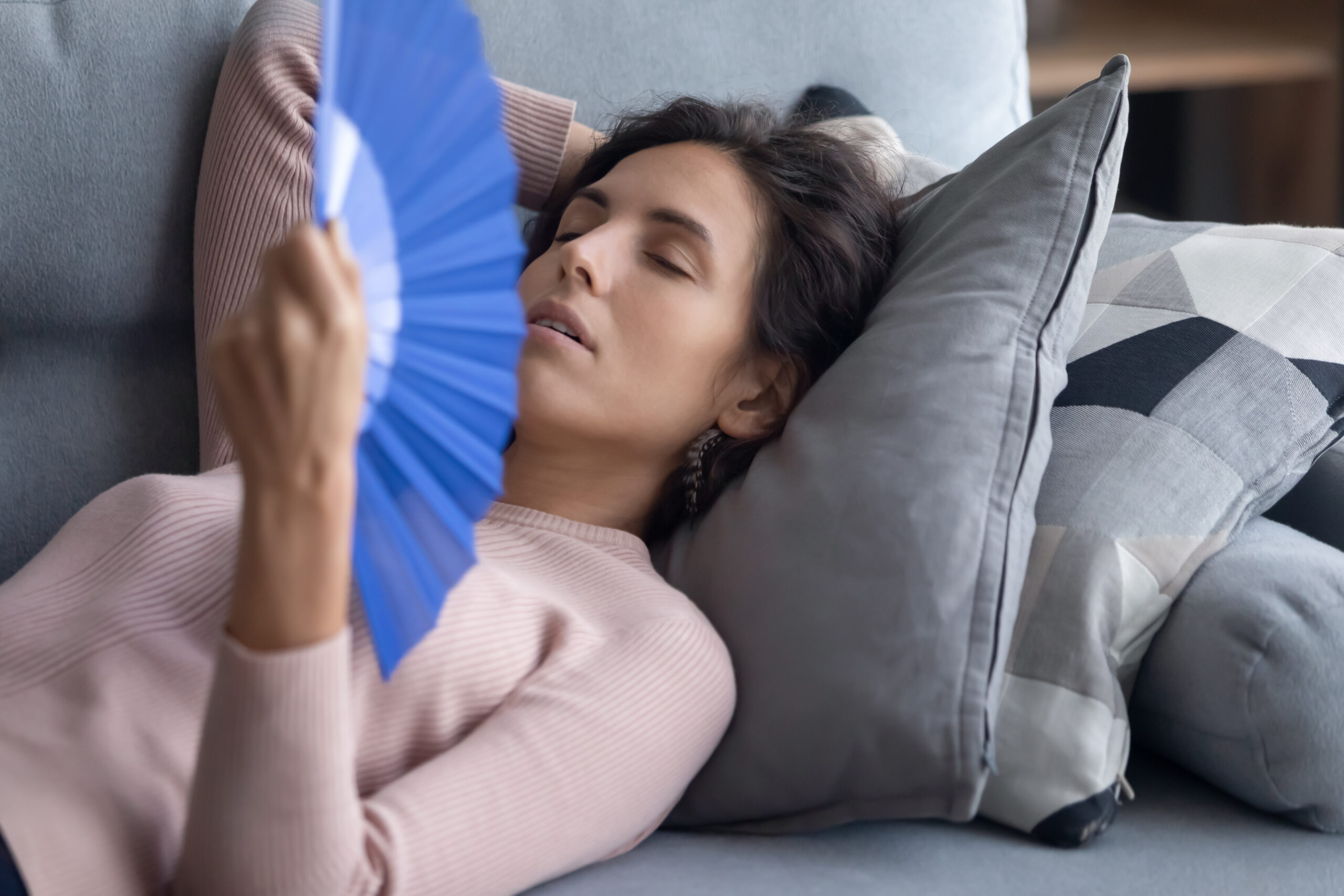 a woman fanning herself to cool down while trying to sleep