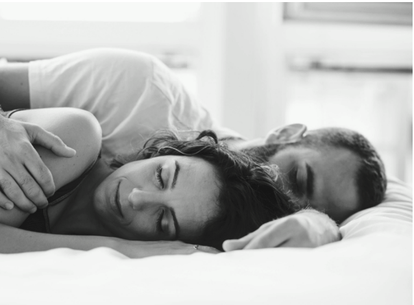 A man and a woman sleeping on their sides in bed