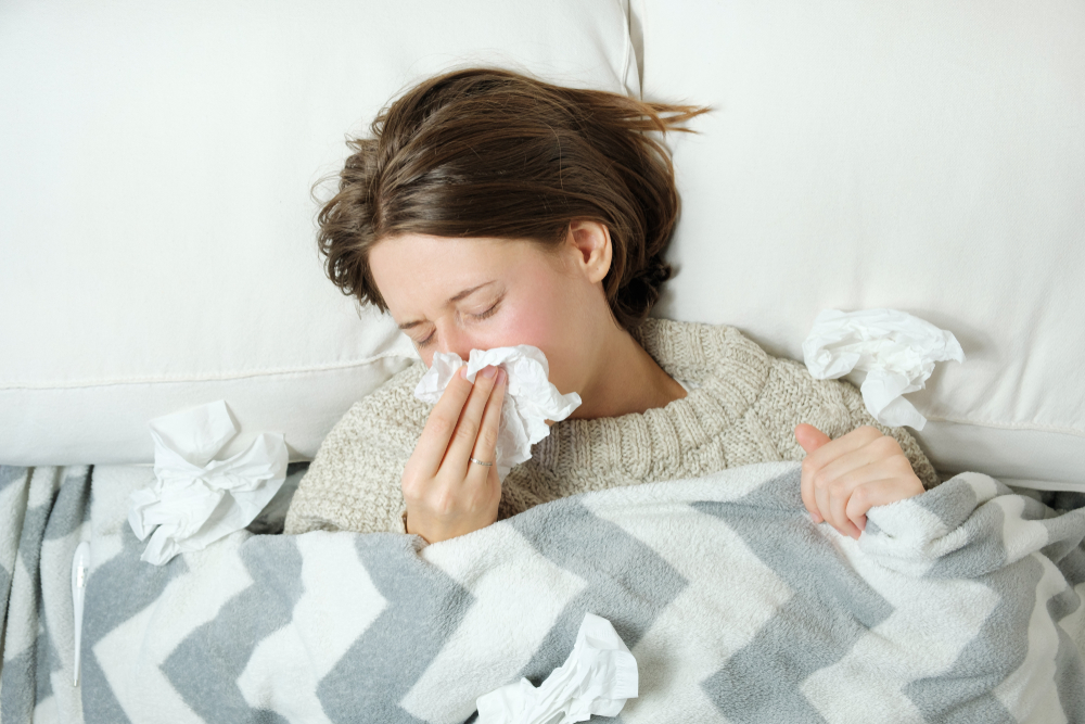 A woman blows her nose while in bed, wondering how to help hay fever at night